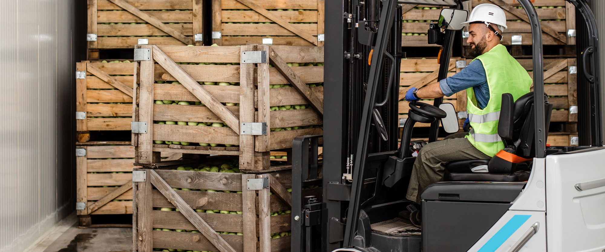 Forklift operator in a high-visibility vest moving crates of produce in a warehouse